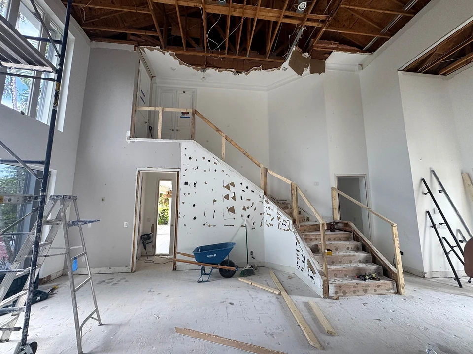 The same staircase during demolition with ceiling framing exposed and temporary handrails